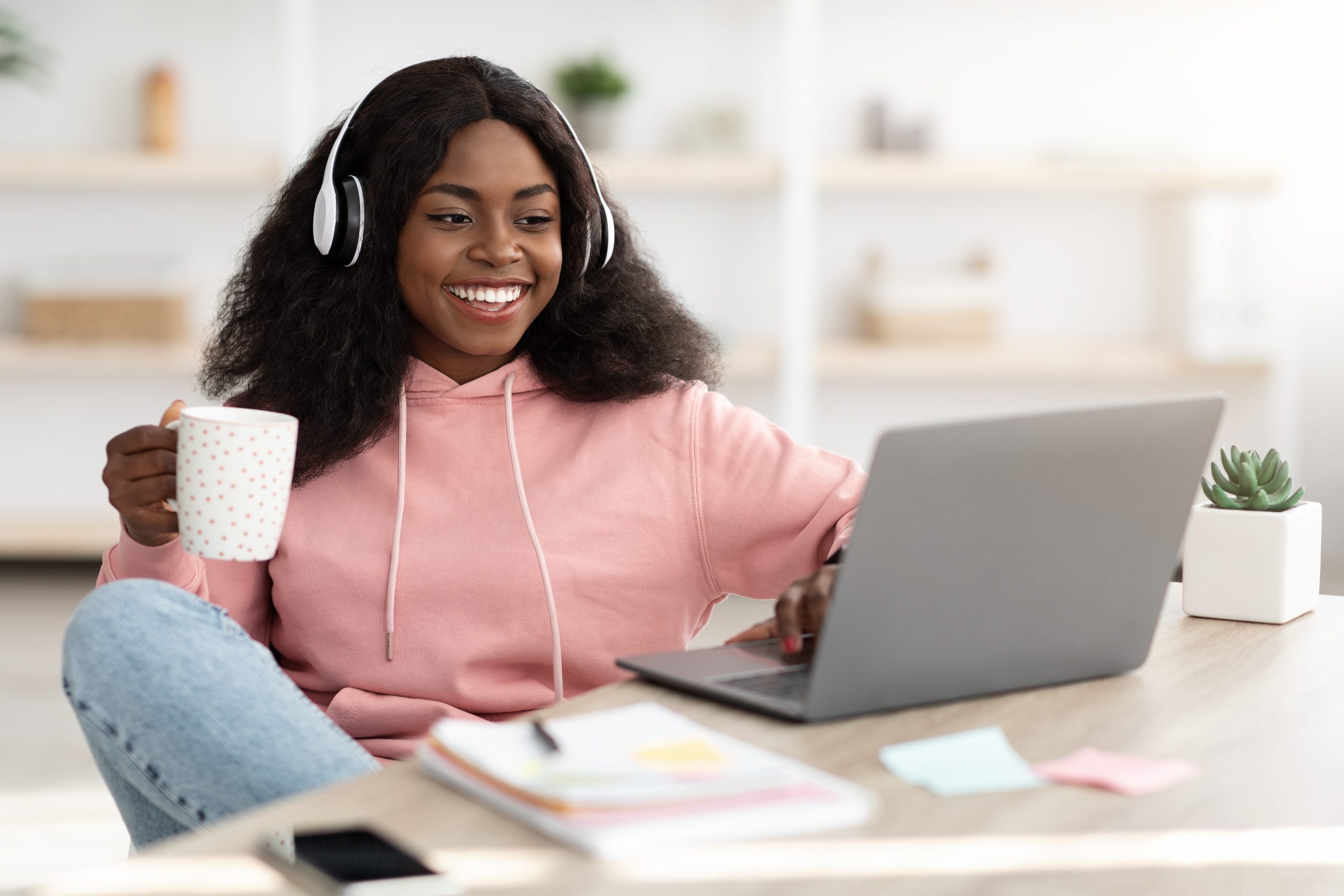 Joyful black lady watching movie online, using laptop at home